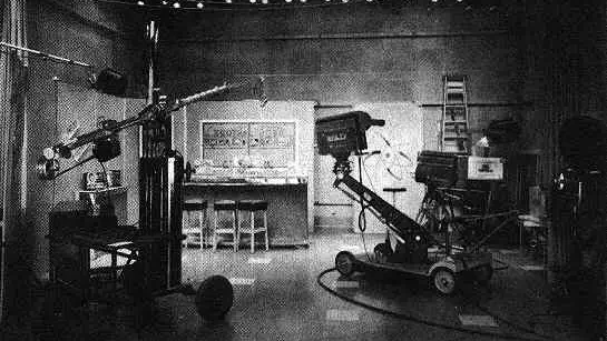 An empty television dance studio with a polished floor, cameras on wheeled stands, overhead studio lights. The room is quiet. The set looks recently used but now vacant.